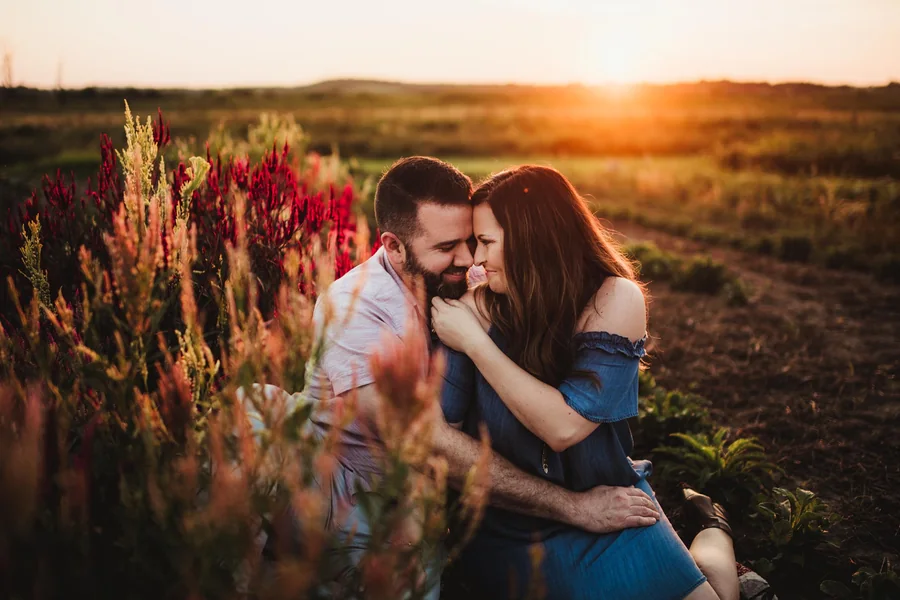 A couple lean together among tall flowers in warm sunset light.