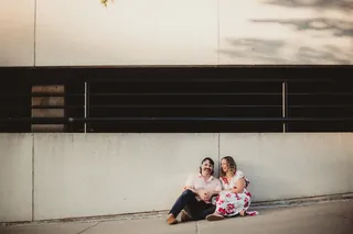 Two people sit together against a simple wall in a wide frame.