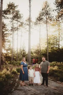 A family of four stands together on a tree-lined path, with the setting filling much of the frame.