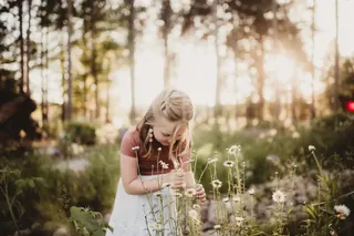 A young child leans toward small flowers in a garden.