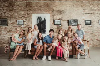 A group sits closely together on a couch against a brick wall.