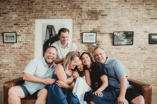 Several adults lean together and laugh while seated on a couch.