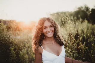 A senior smiling among tall grasses in warm evening light.