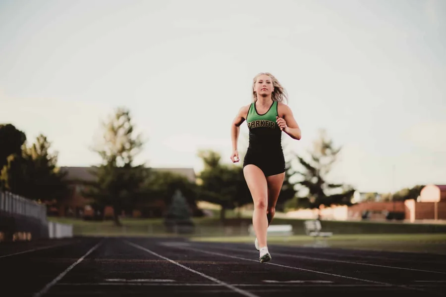 A senior sprinter in a green and black uniform running on a track at dusk.