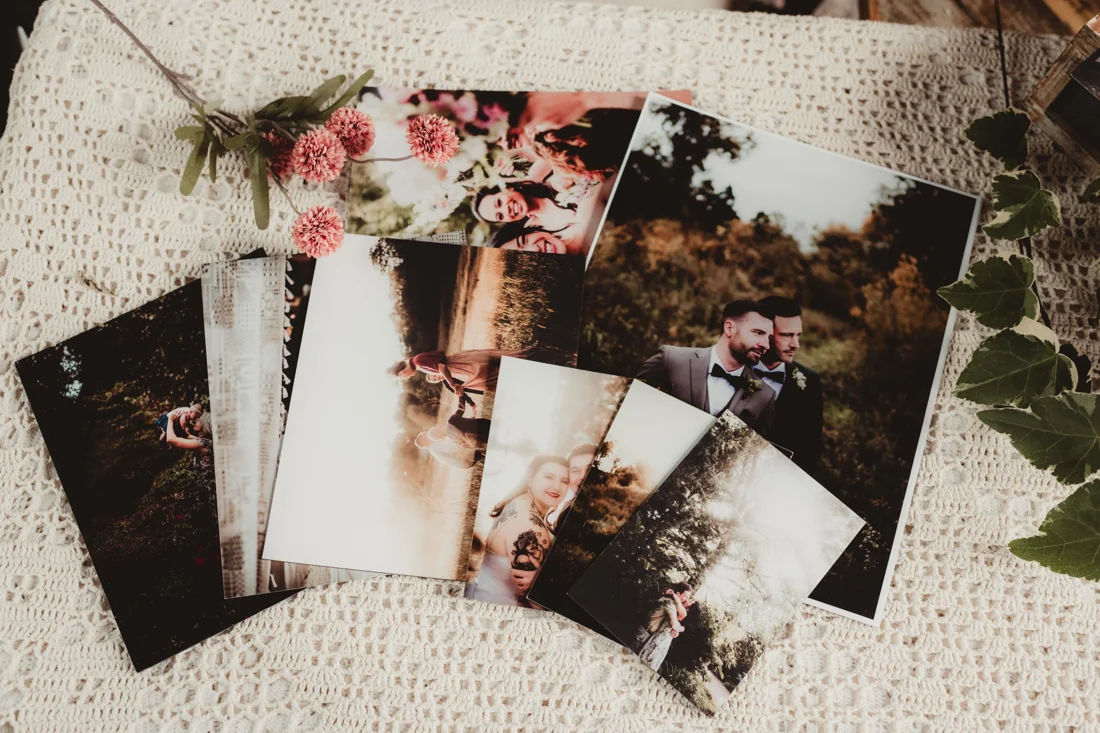Printed wedding and couple photographs fanned out on a cream crochet cloth, with flowers and ivy.