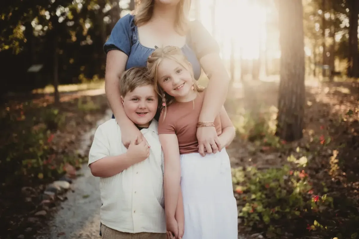 Two children smiling beside their mother outdoors