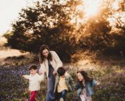 A joyful mother and her three children running through a field of wildflowers at sunset, showcasing the techniques taught in the Family Photography Online Workshop.