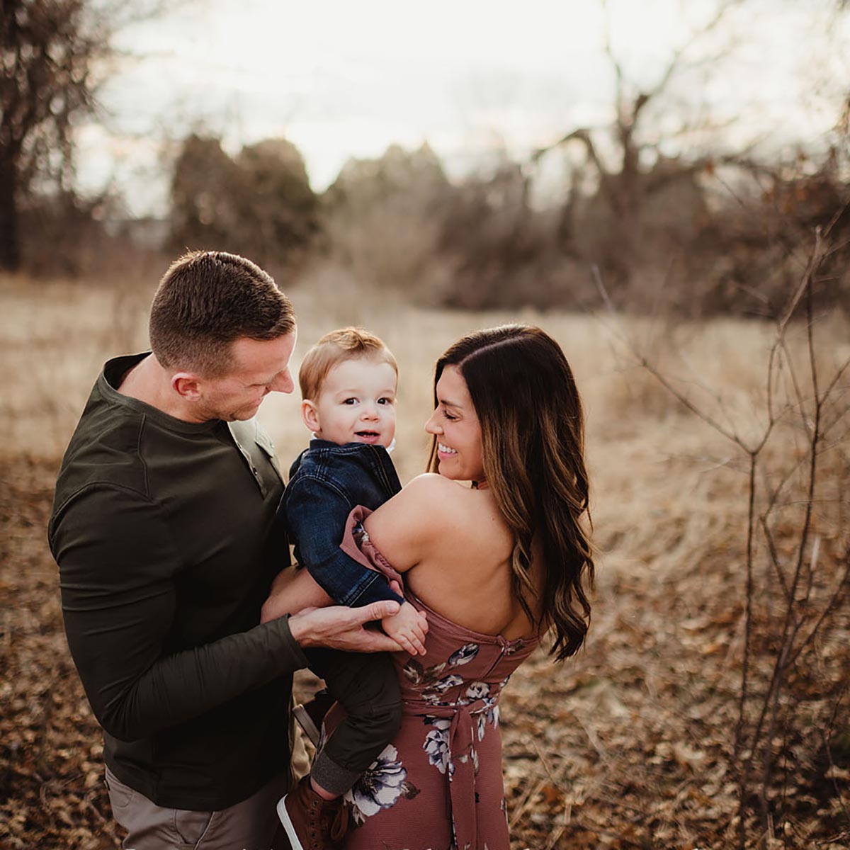 A child held between his parents in soft outdoor light