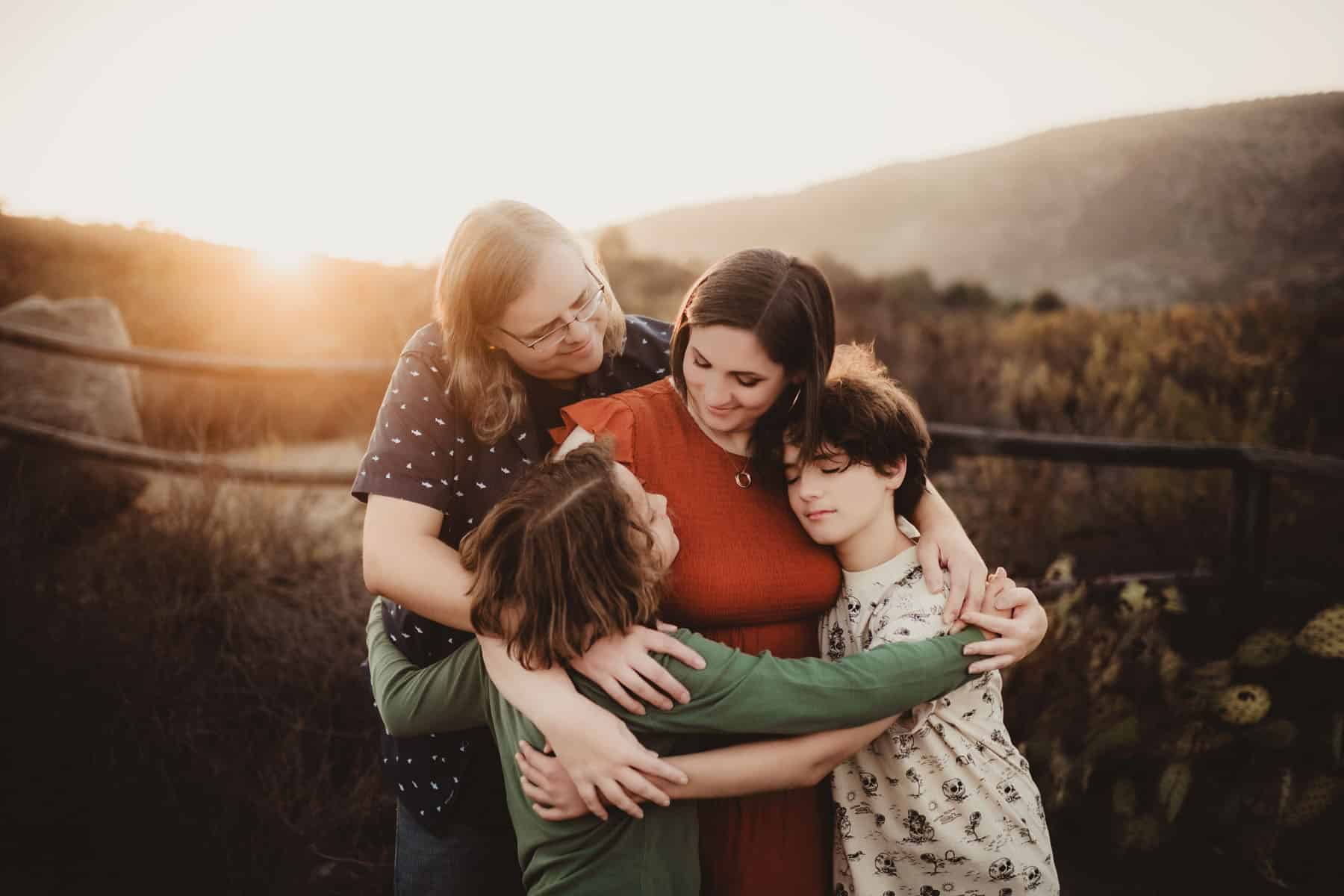 A family of four sharing a warm embrace at sunset in a rustic nature setting with cactus plants and hills in the background