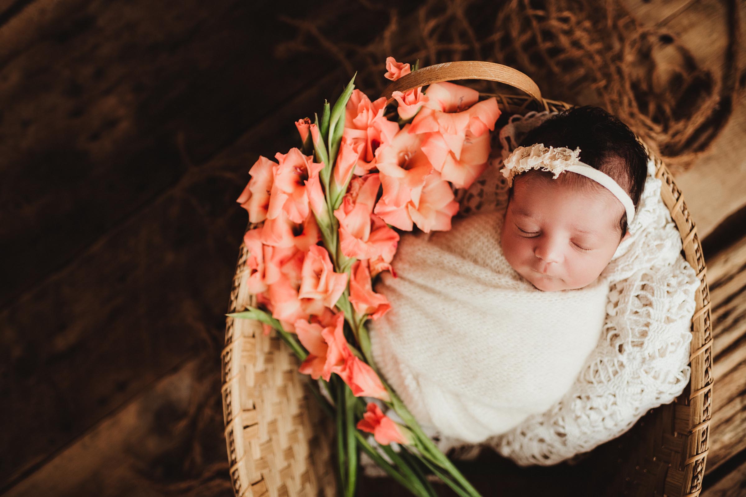 infant wrapped in an open basket with peach flowers