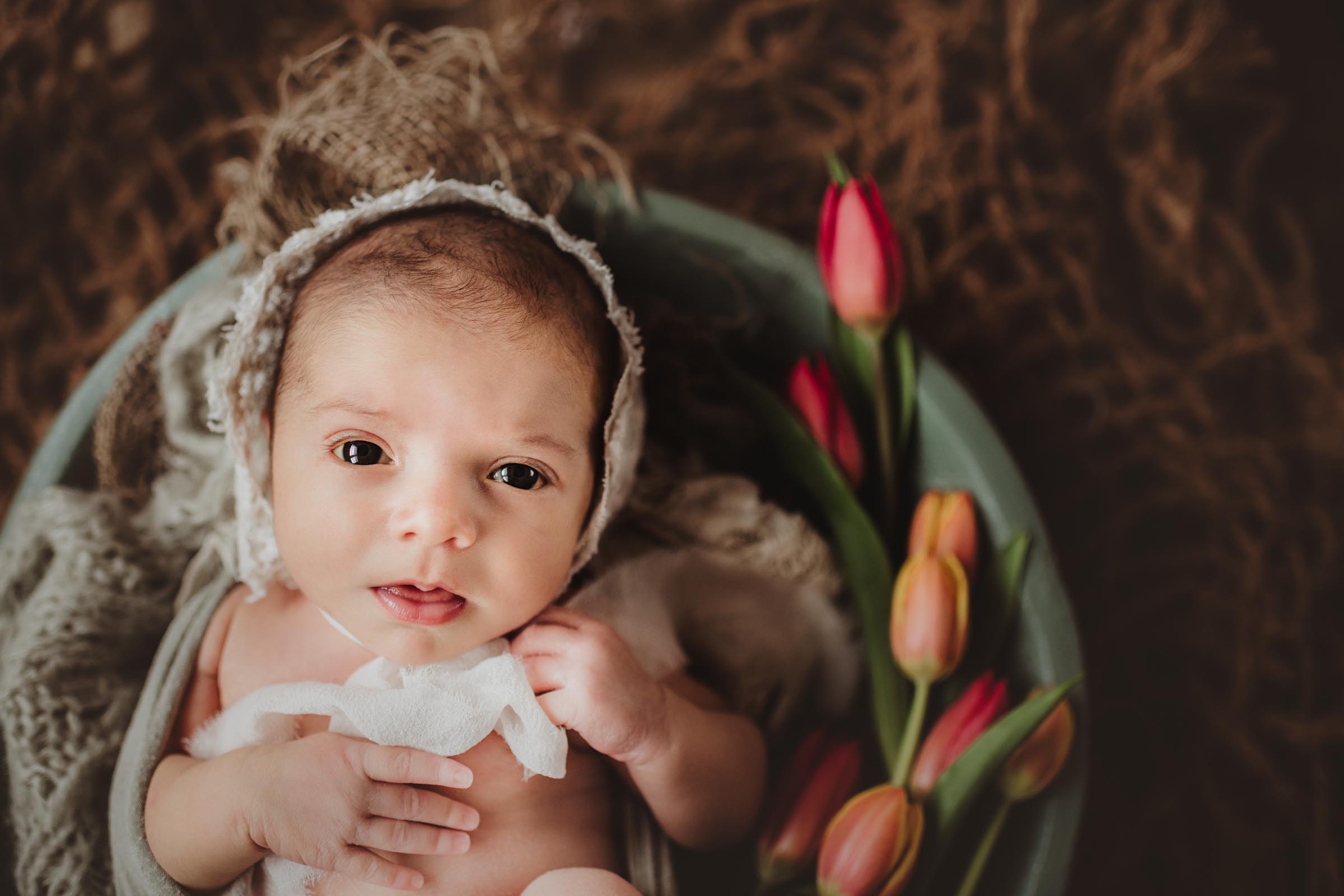 awake baby in wooden bowl with flowers