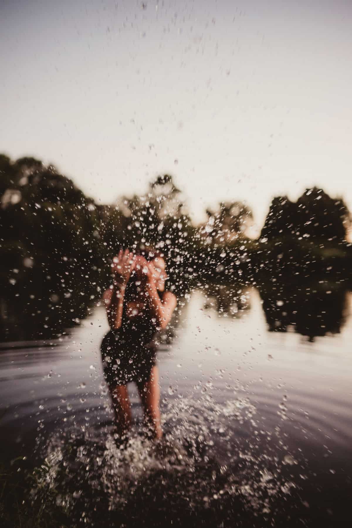 Blurred figure of a person throwing water in the air, with water droplets frozen mid-air against a soft-focus natural background.