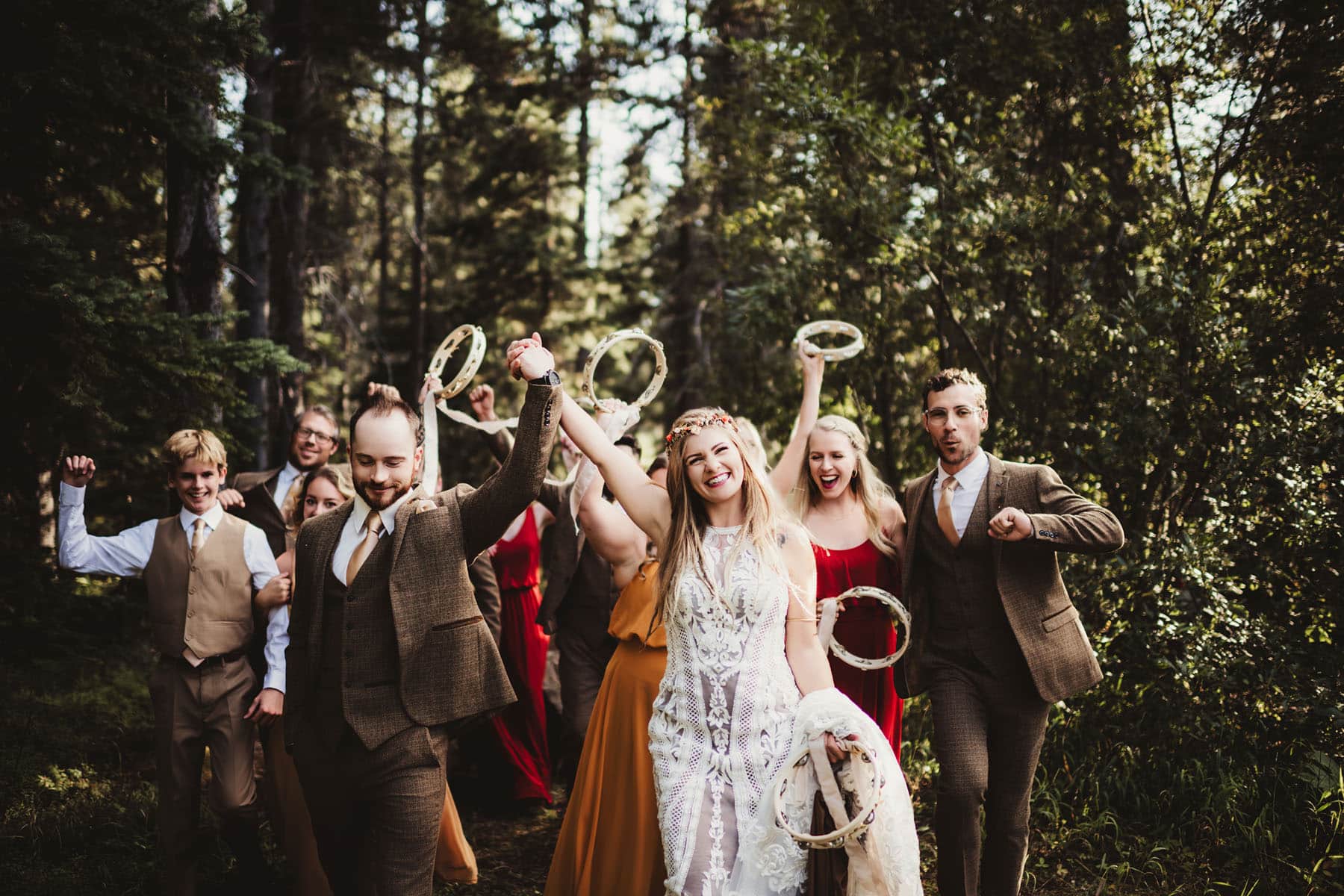 A joyful group of wedding guests in a forest, waving tambourines and celebrating with the bride and groom.