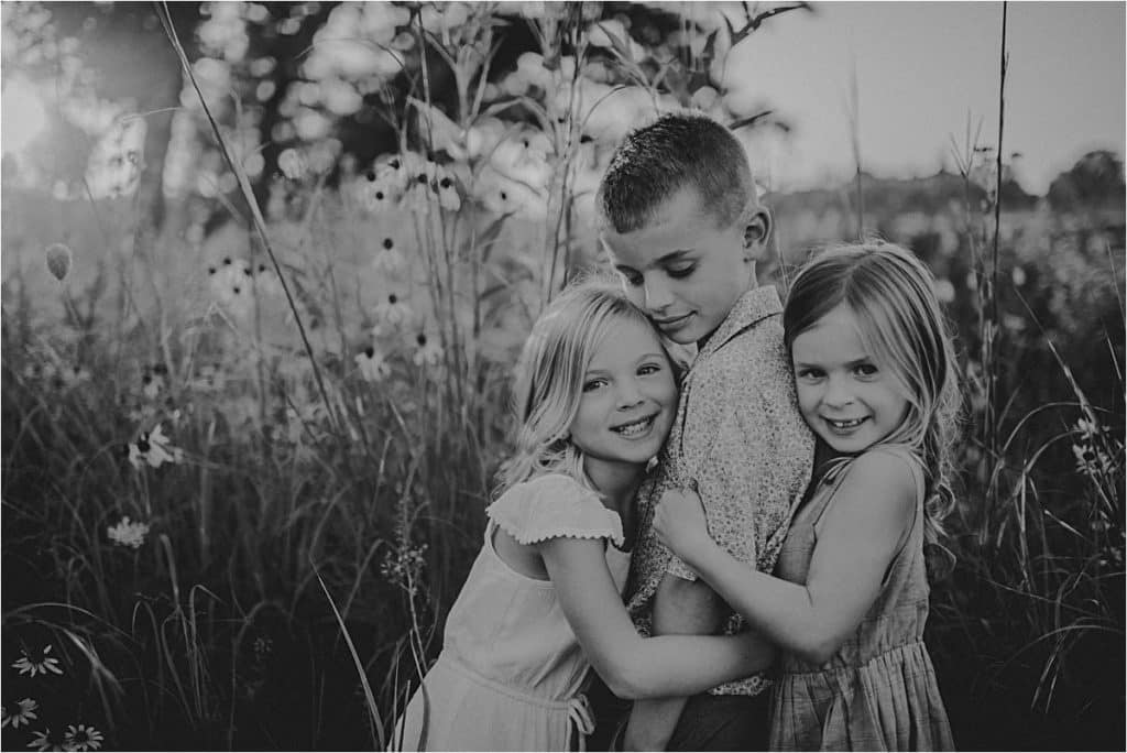 Summer Wildflower Sibling Session Sisters Hugging Brother