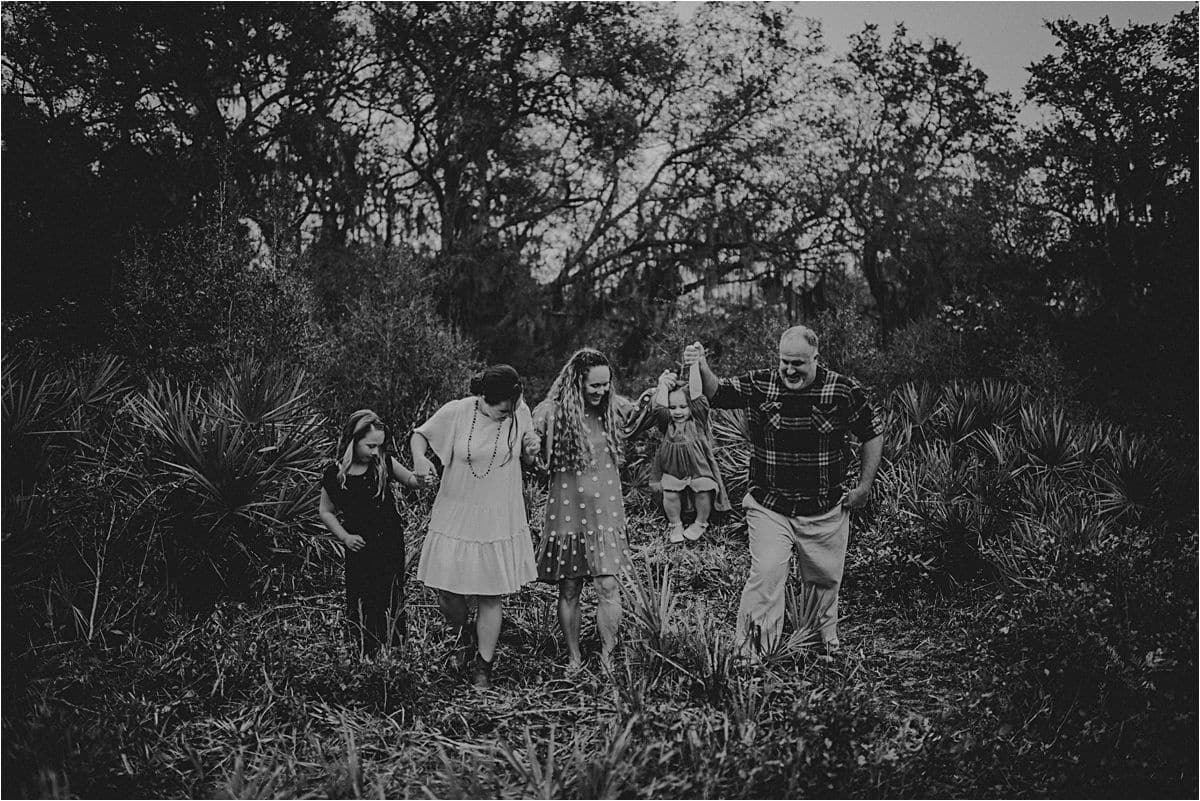 Family of five walks hand in hand through palmetto brush under oaks in black and white