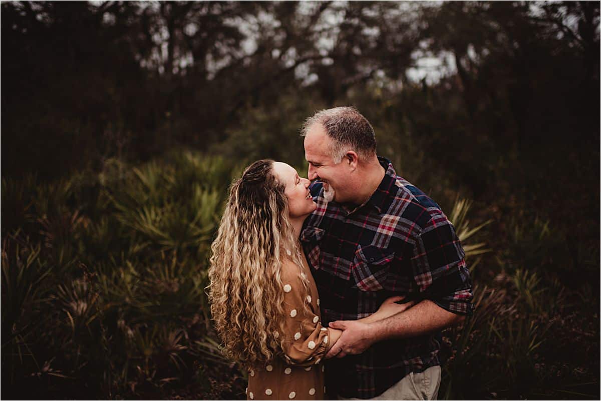 Mom and dad laugh and embrace surrounded by palmetto palms during a family photography session