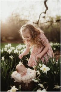 Spring Outdoor Newborn Session Sister Putting Flower on Baby's Head