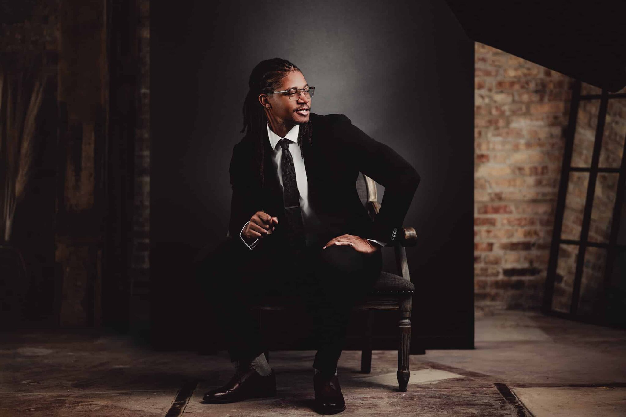 Man in a dark suit and glasses seated beside exposed brick