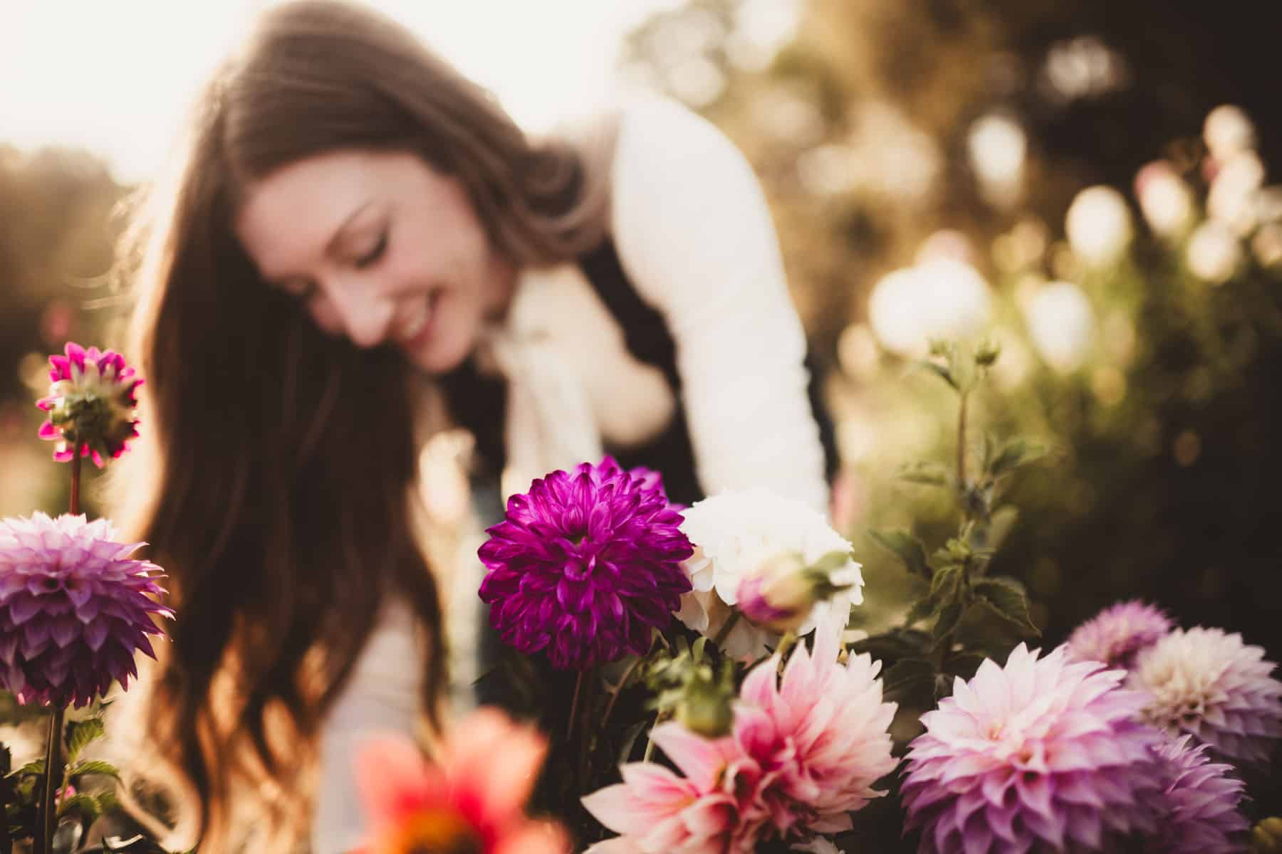A florist bending over smelling vibrant purple flowers in a sunlit garden