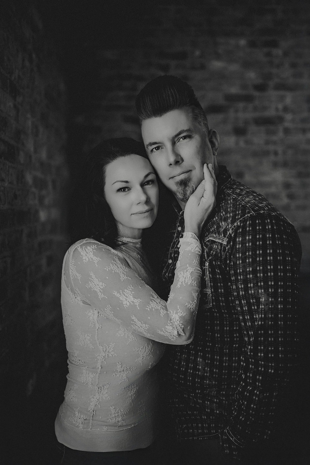 Black and white photo of Doug an Courtney embracing, with the man gently holding the woman's face against a brick background