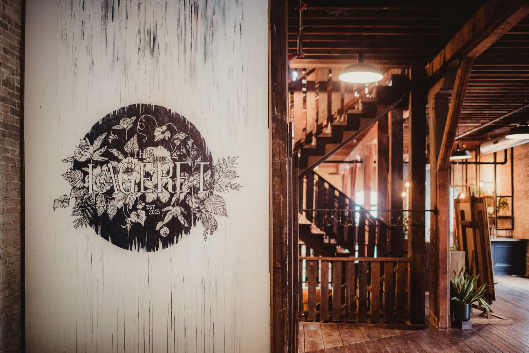 Vintage styled mural with 'The Jageret, Est 2015' logo on a distressed white wall inside a rustic brewery with exposed brick and wooden elements.