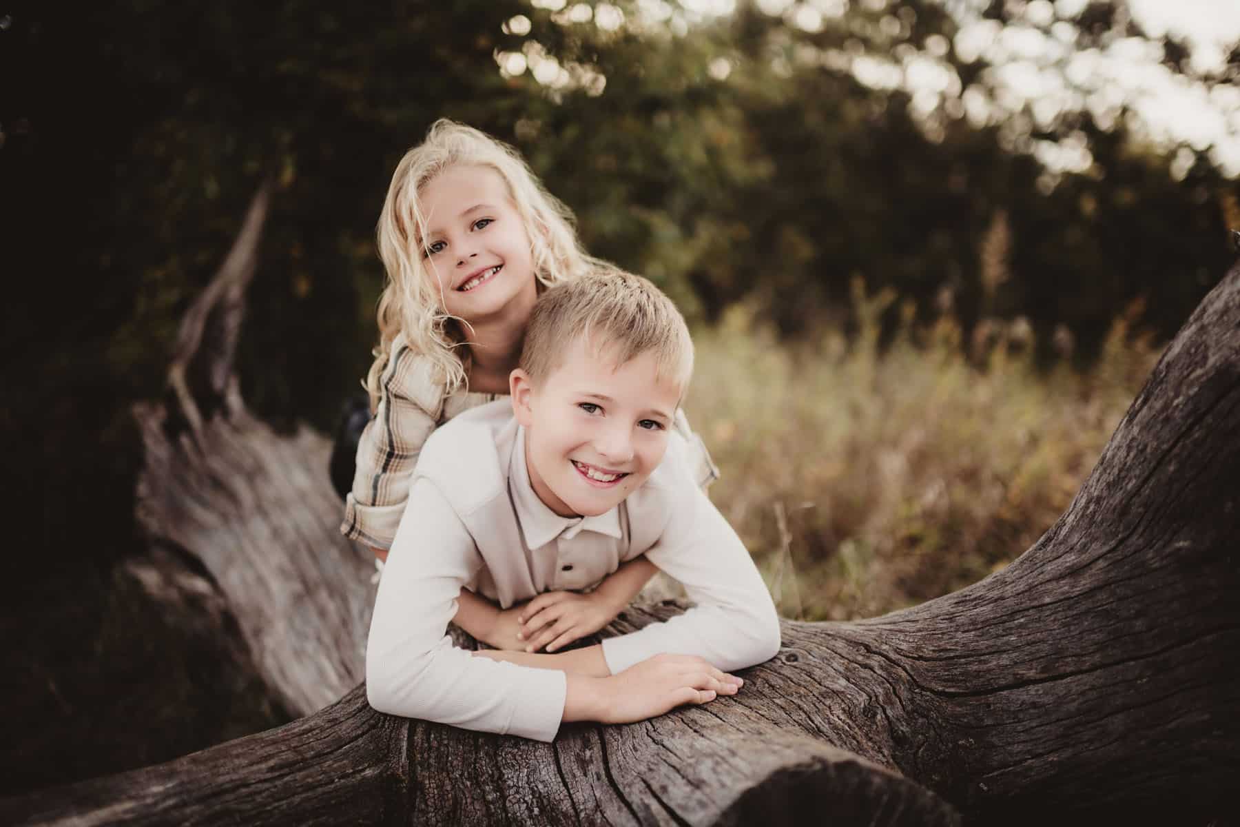 A joyful young boy and girl smiling while lying on an old tree trunk in a natural setting