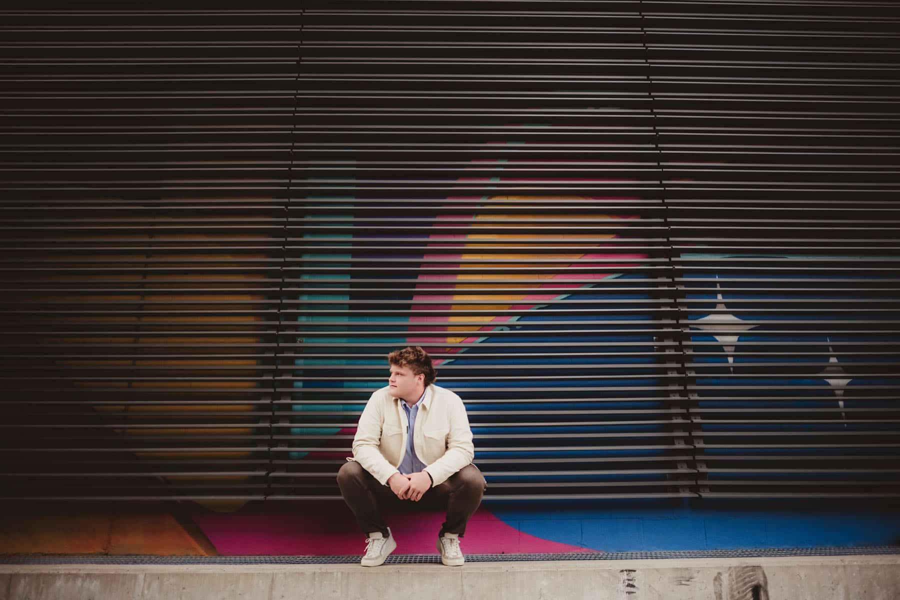 A young man sitting thoughtfully in front of a colorful graffiti wall