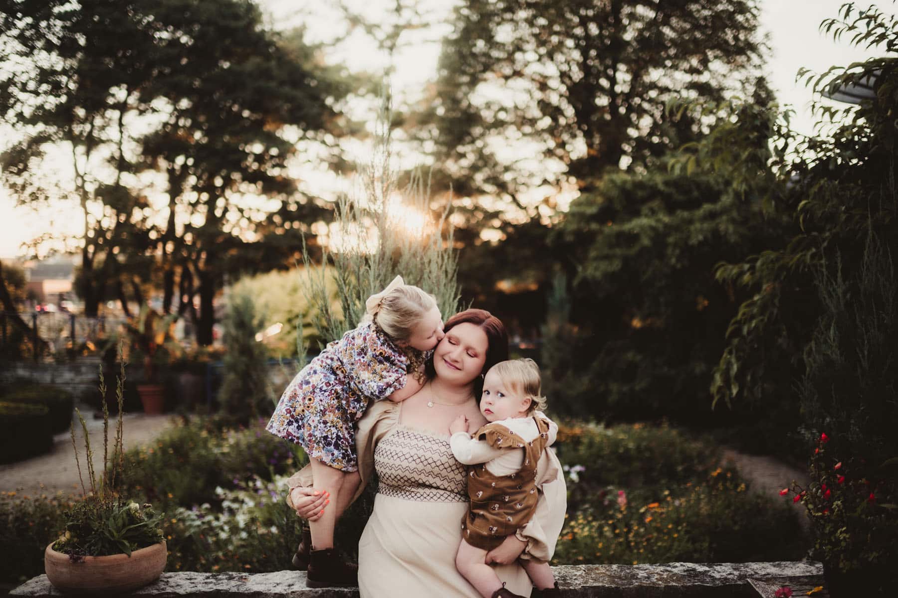 A mother and her two children lovingly embracing in a lush garden at sunset