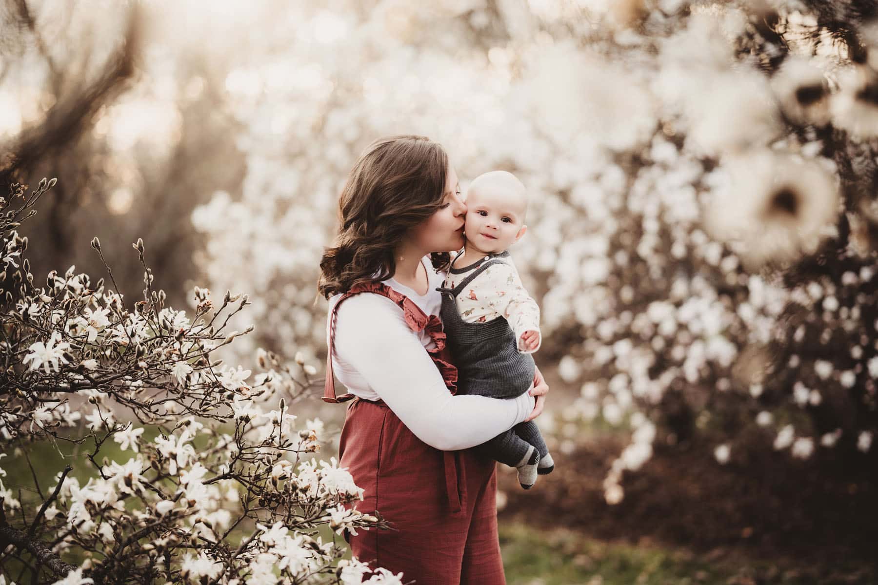 A mother gently kissing her baby's cheek amidst vibrant springtime blossoms