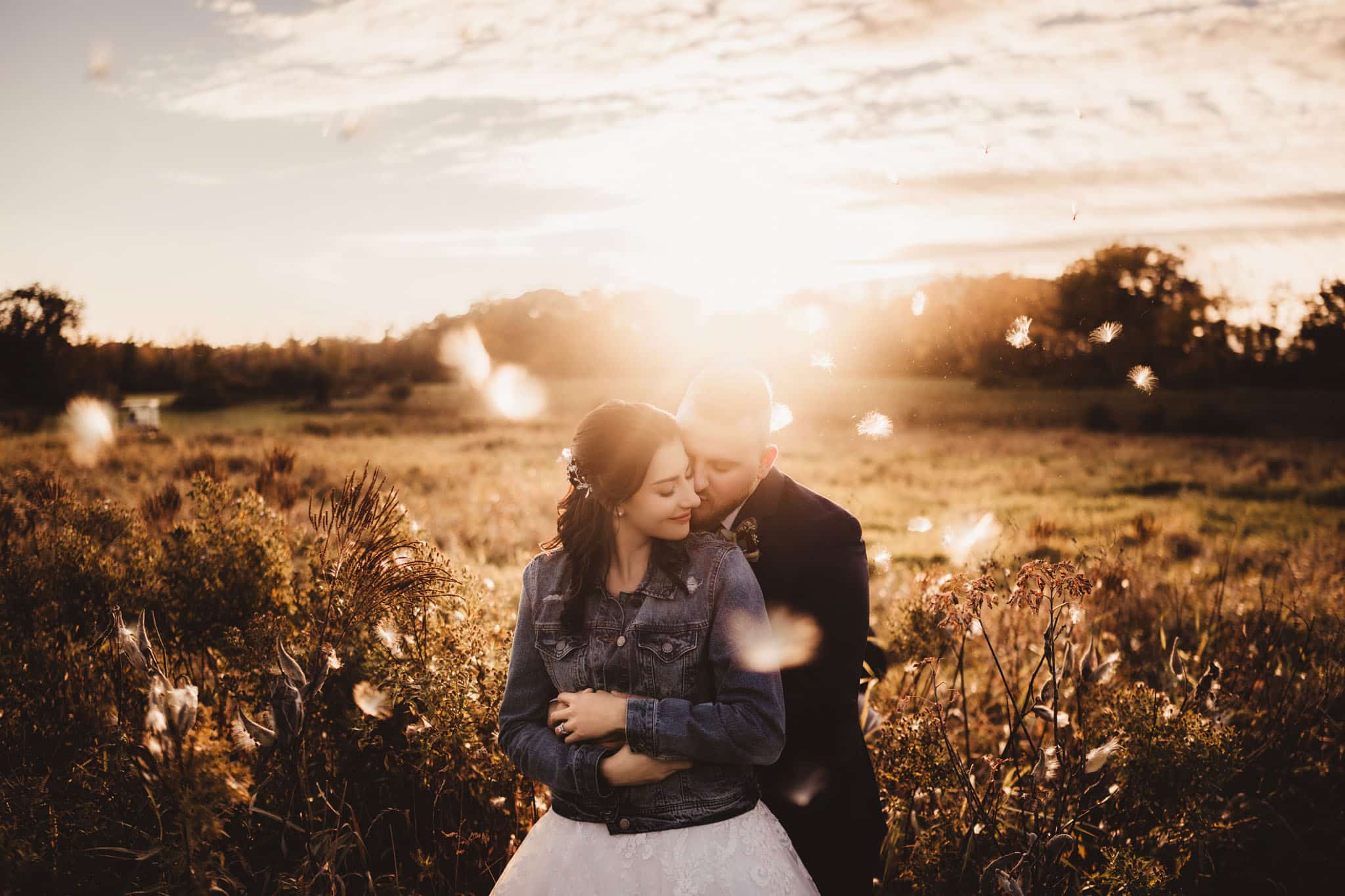 romantic_sunset_couple_photo_shoot Couple embracing in a sunlit field at sunset, surrounded by nature and floating dandelion seeds