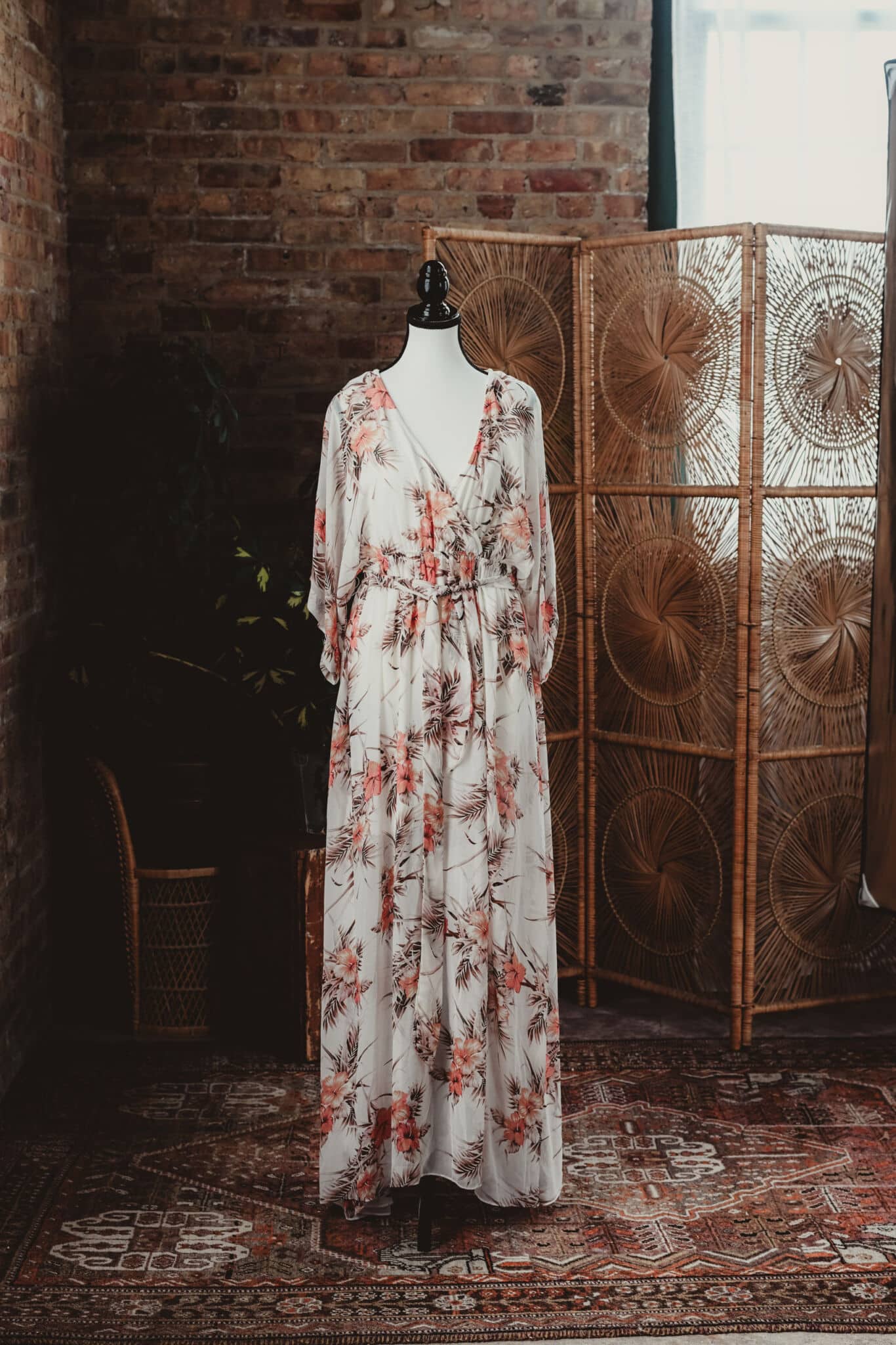 Elegant floral dress on a mannequin in a vintage room with a brick wall and rattan screen