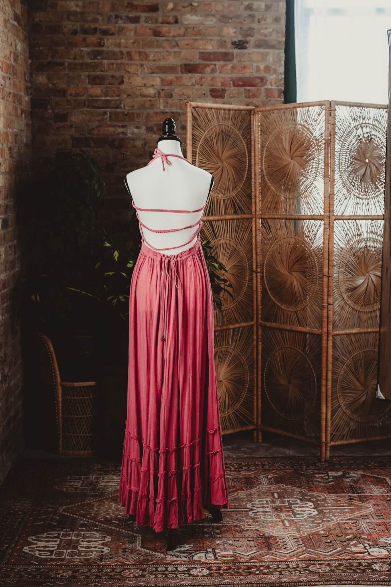 A pink vintage dress displayed on a mannequin in a loft with rustic brick wall and a decorative rattan screen.