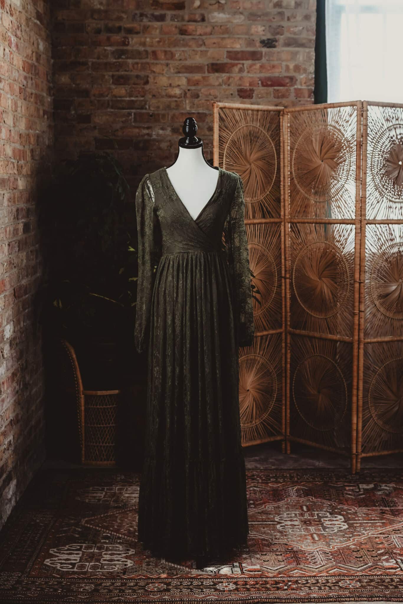Vintage green velvet dress on a mannequin against a brick wall with a patterned folding screen and Persian rug in the background