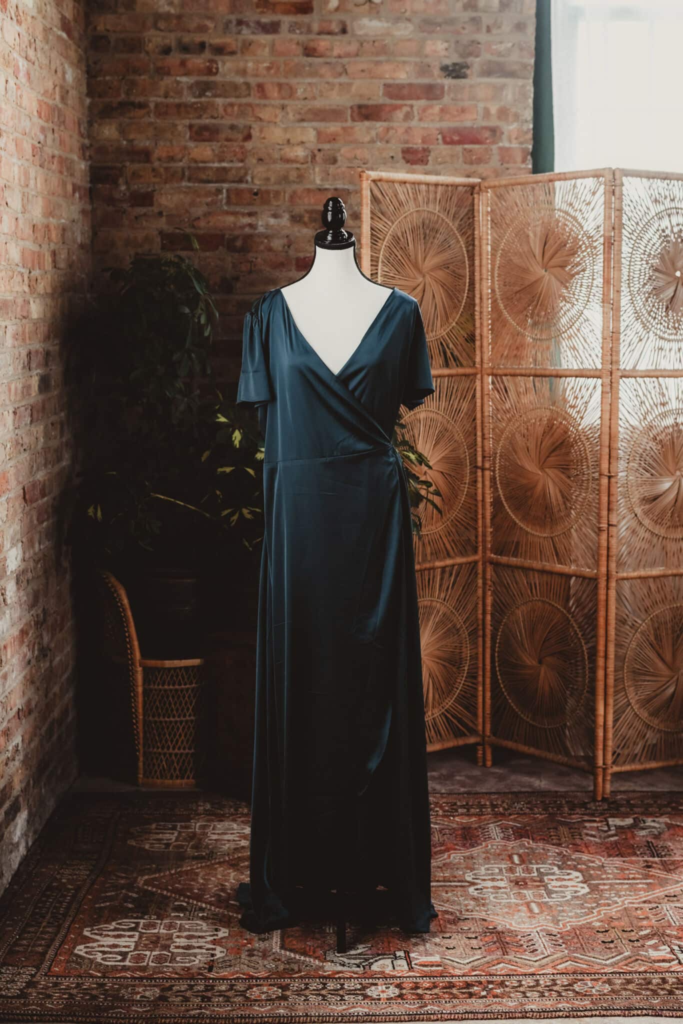 An elegant blue dress displayed on a mannequin in a vintage-styled room with brick walls and a wicker partition