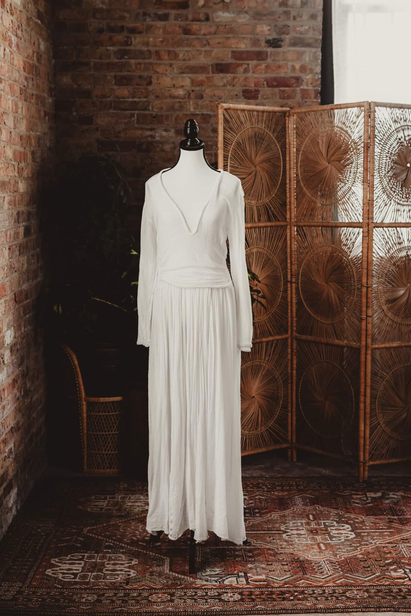 A mannequin dressed in an elegant white long dress displayed in a rustic room with a brick wall and vintage decor