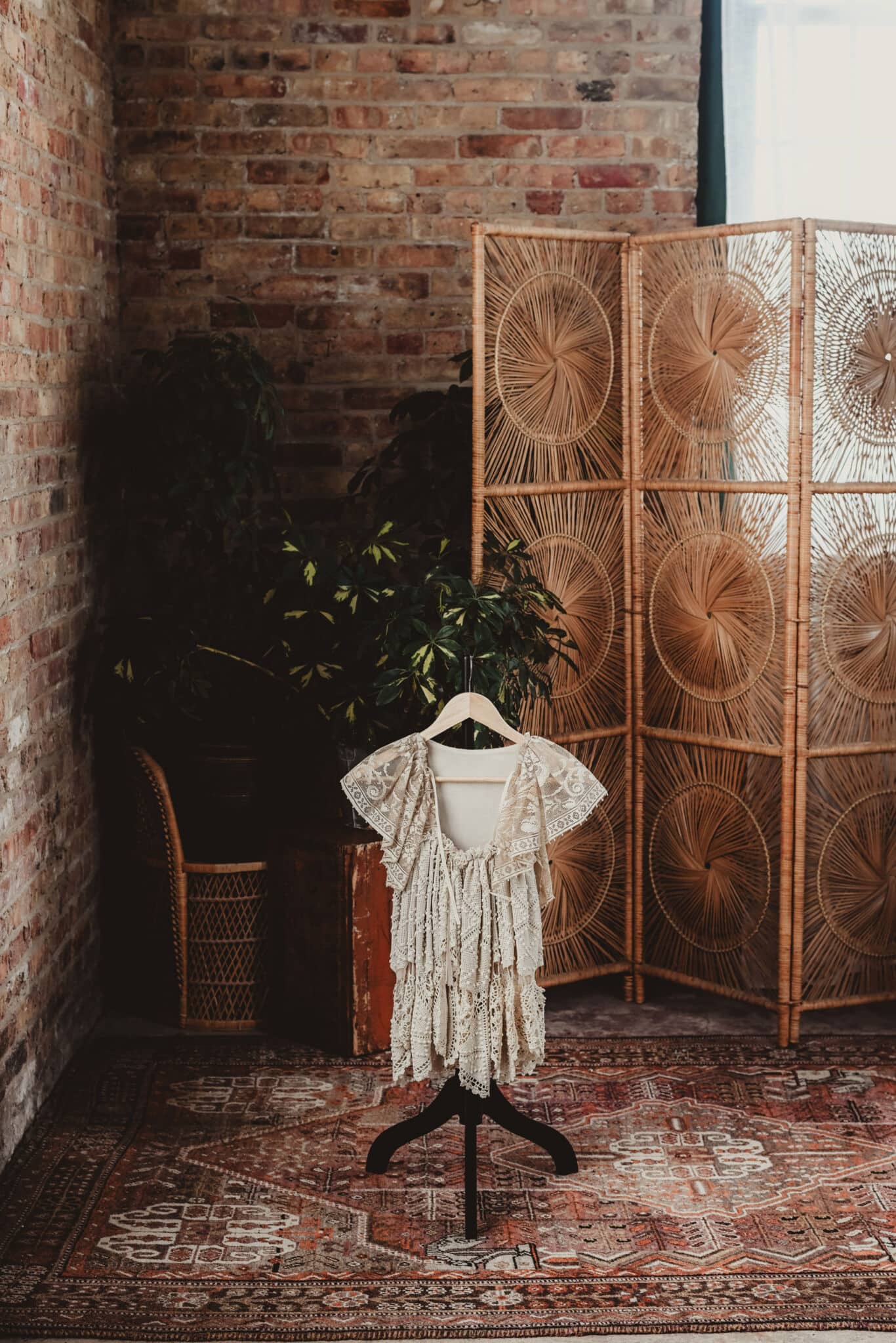 A vintage lace dress on a mannequin in a stylish room with brick walls and a rattan room divider.