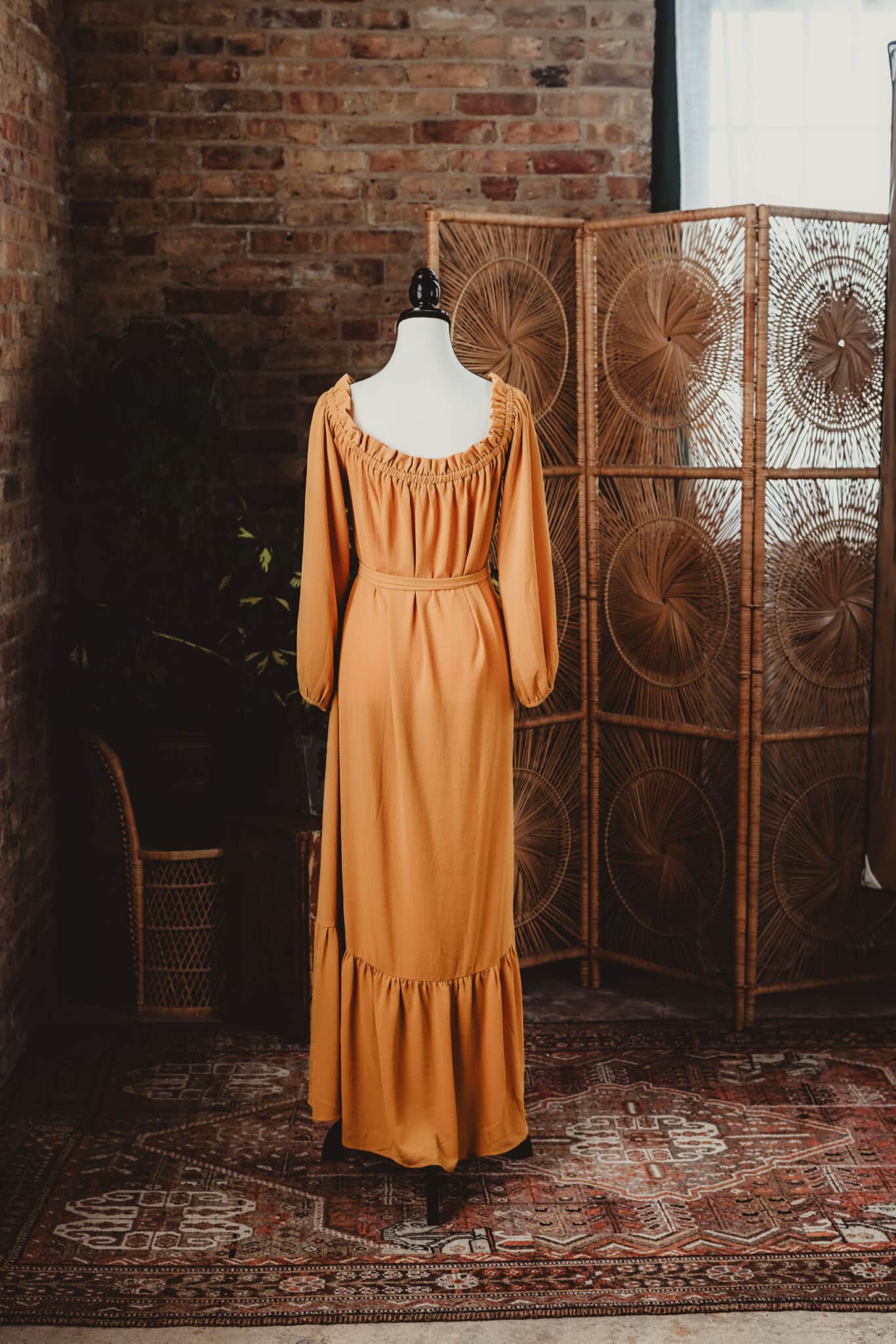 Vintage orange dress displayed on a mannequin in a rustic interior with bohemian style wicker dividers and brick wall background.