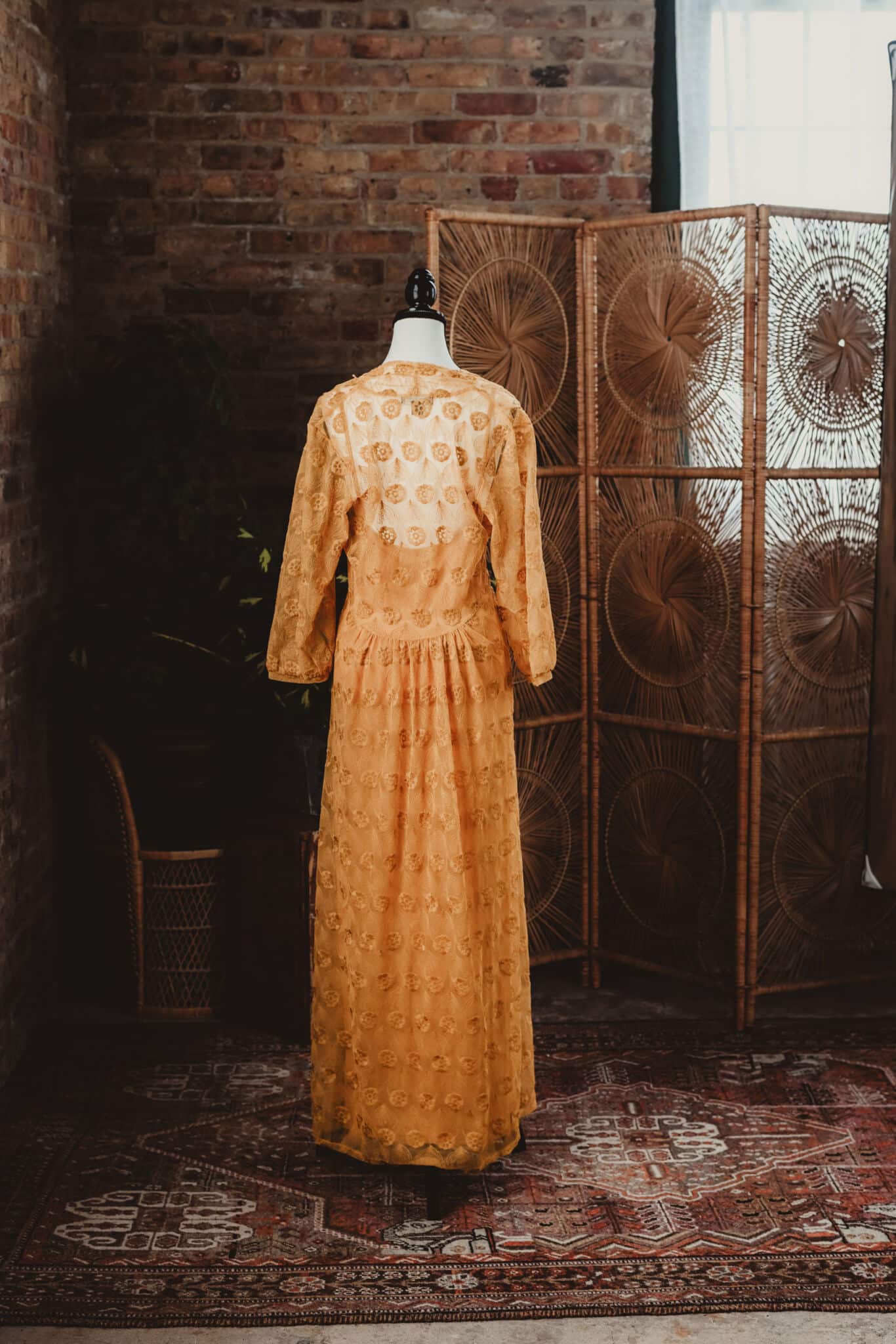 Antique yellow dress displayed on a mannequin in a rustic interior setting with a brick wall and a decorative screen