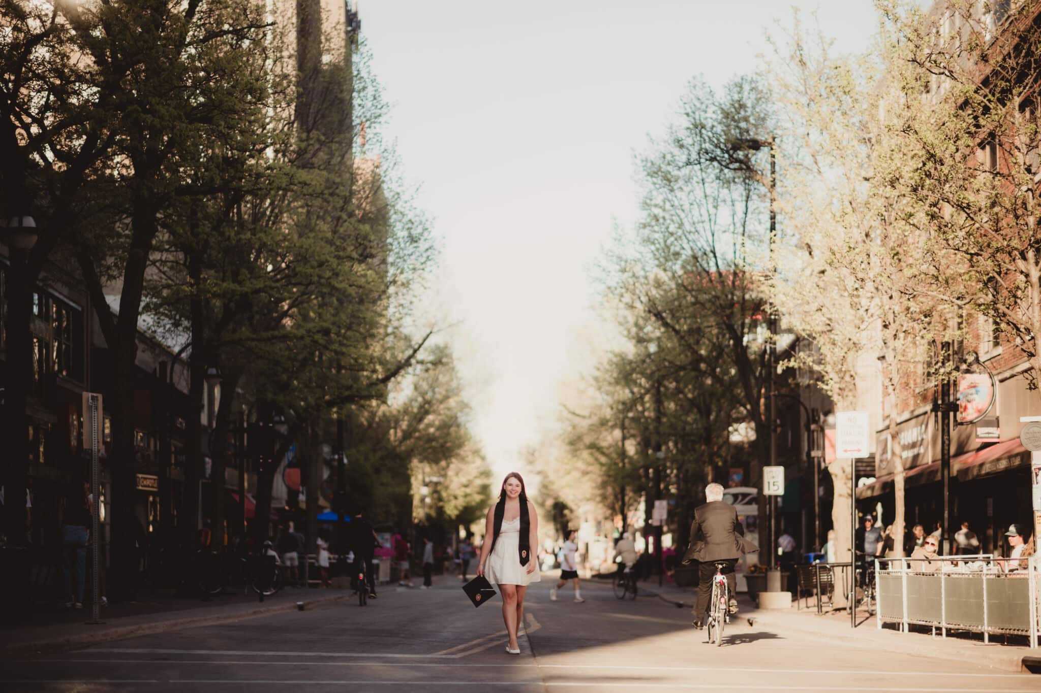 sunny_city_street_scene_with_walking_woman A woman walks down a sunny city street lined with lush trees and busy sidewalk cafes.