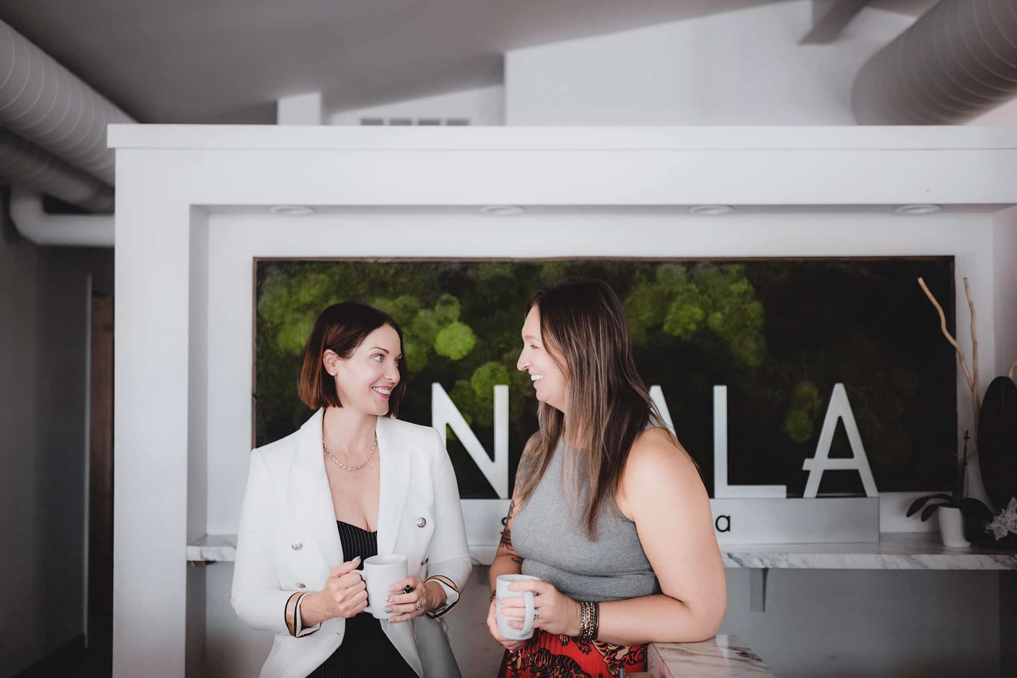 professional_women_enjoying_coffee_break Two professional women engaging in a friendly conversation over coffee in a stylish office