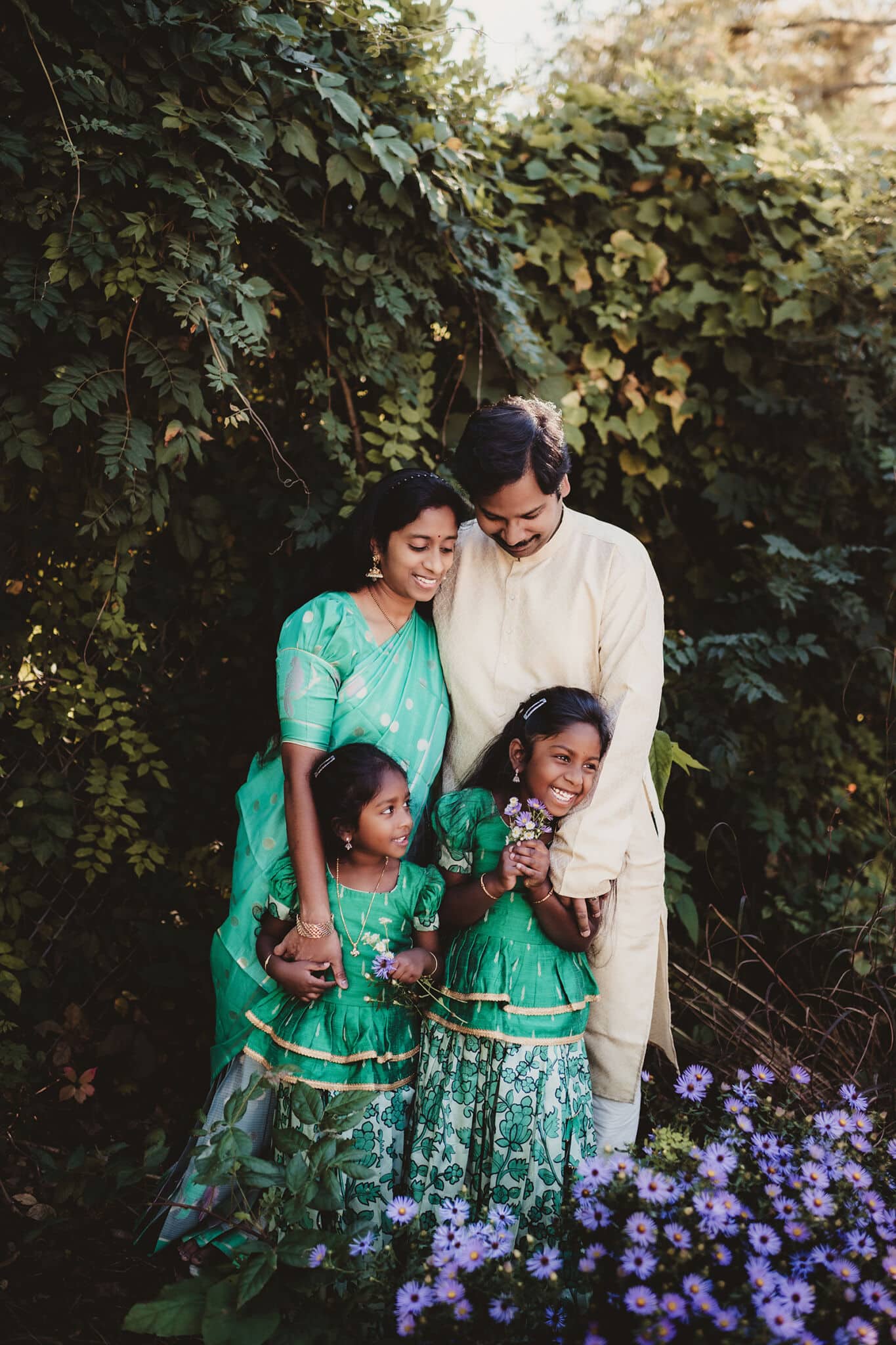 Family of four in coordinating green and cream attire laughing among purple wildflowers during a Madison mini session