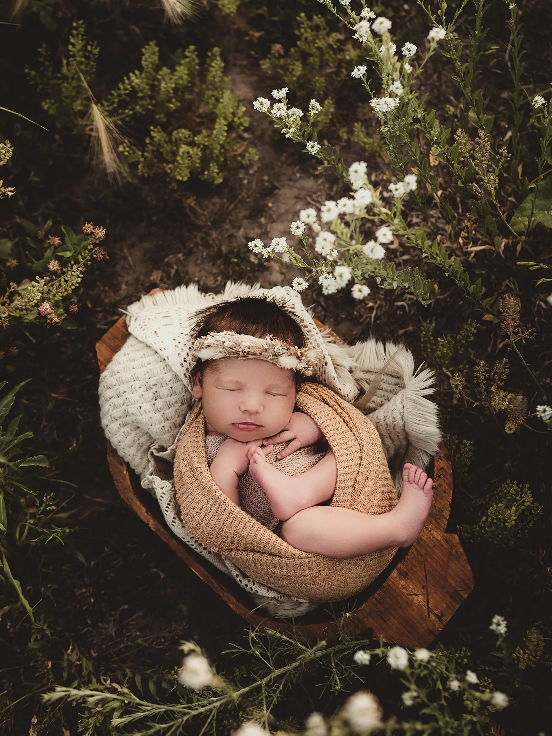 Newborn peacefully sleeping in a cozy blanket nest surrounded by wildflowers and greenery for newborn photography in Madison Wisconsin