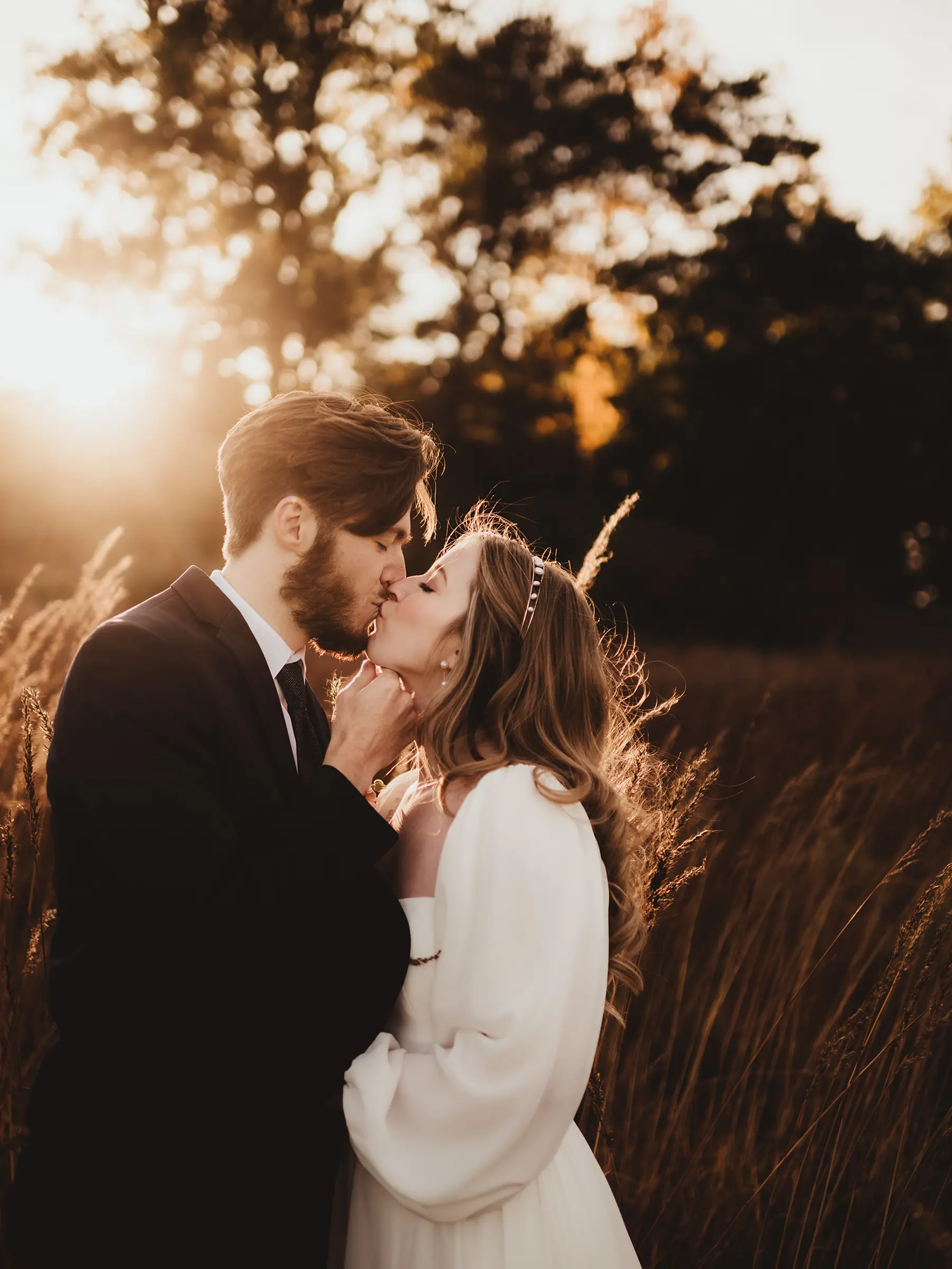 Bride and groom sharing a tender kiss in a sunlit field surrounded by tall grass and autumn trees for Wisconsin wedding photography