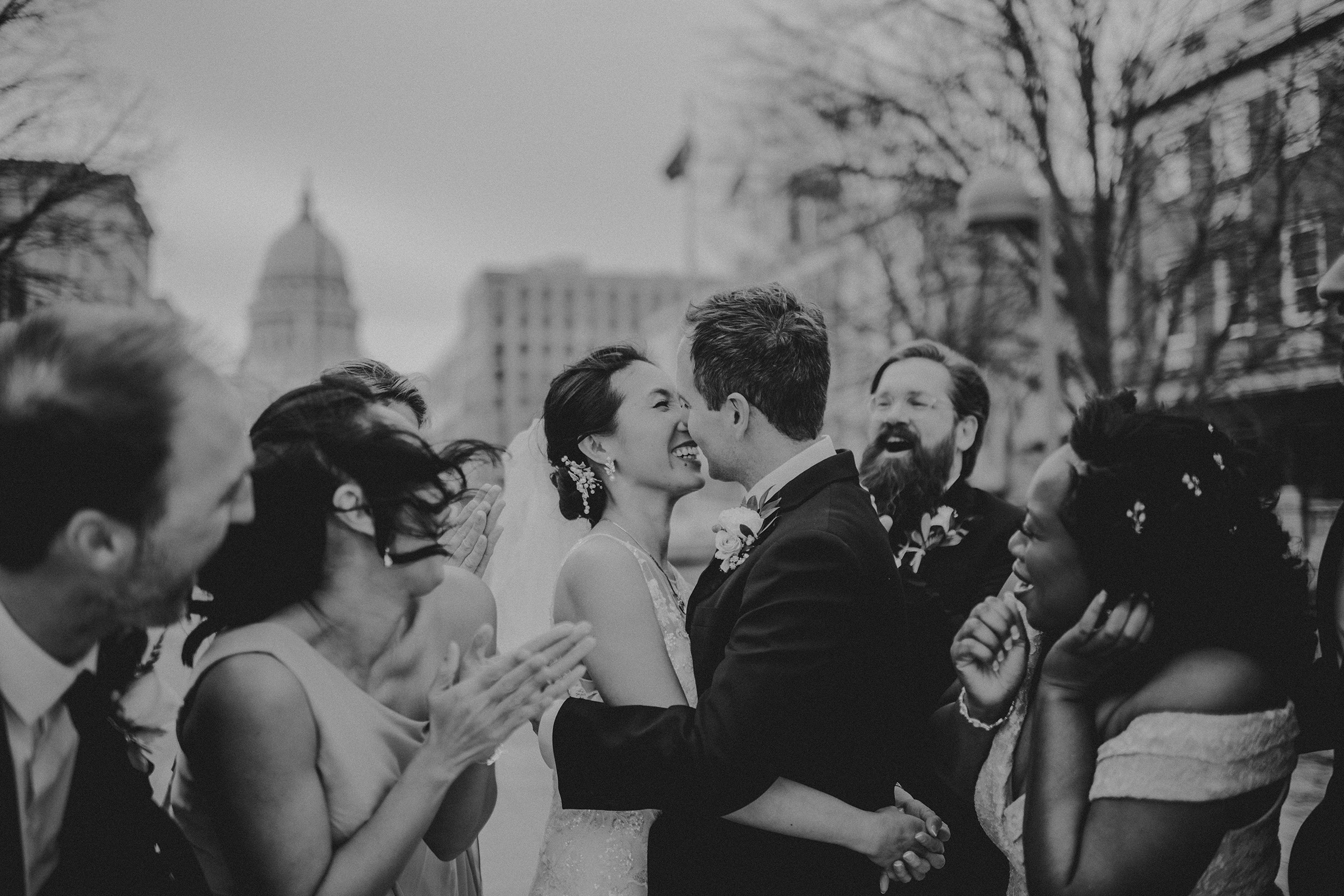 Bride and groom embrace joyfully surrounded by their delighted wedding party, showcasing genuine emotions on their special day.