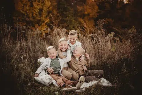 Four children sit together on a blanket in a field of tall grass.