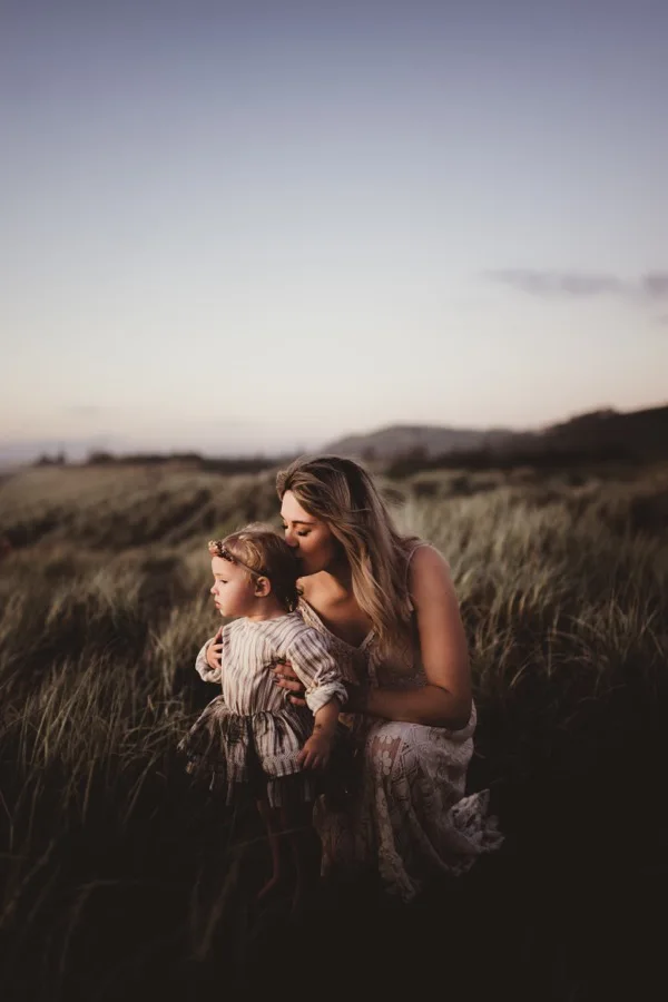An adult and child close together in tall grass beneath an open sky.