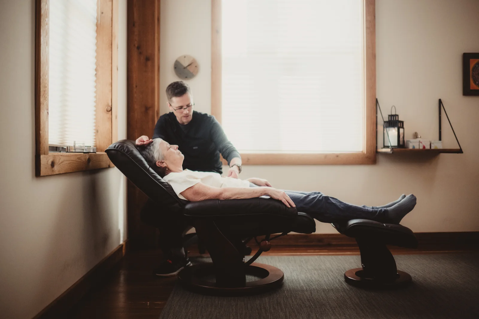 A practitioner works beside a person reclining in a treatment chair.