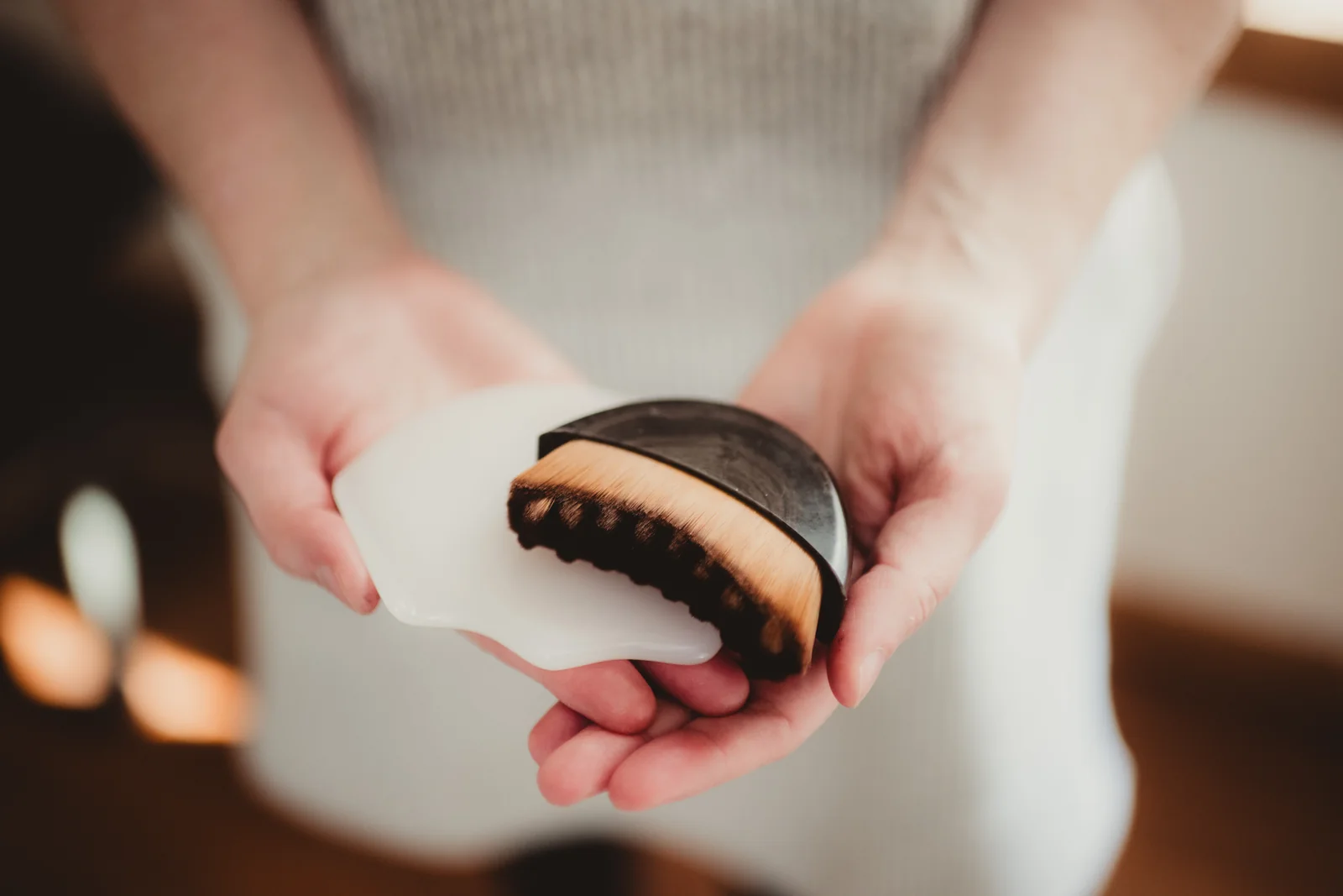 Hands hold a wooden brush and a white treatment tool.