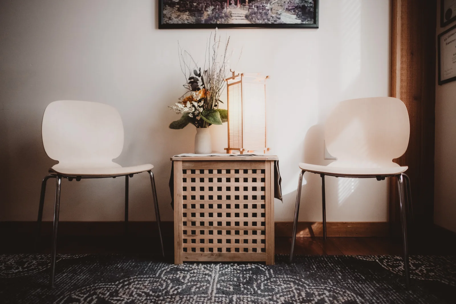 Two white chairs and a small wooden cabinet in a welcoming waiting area.