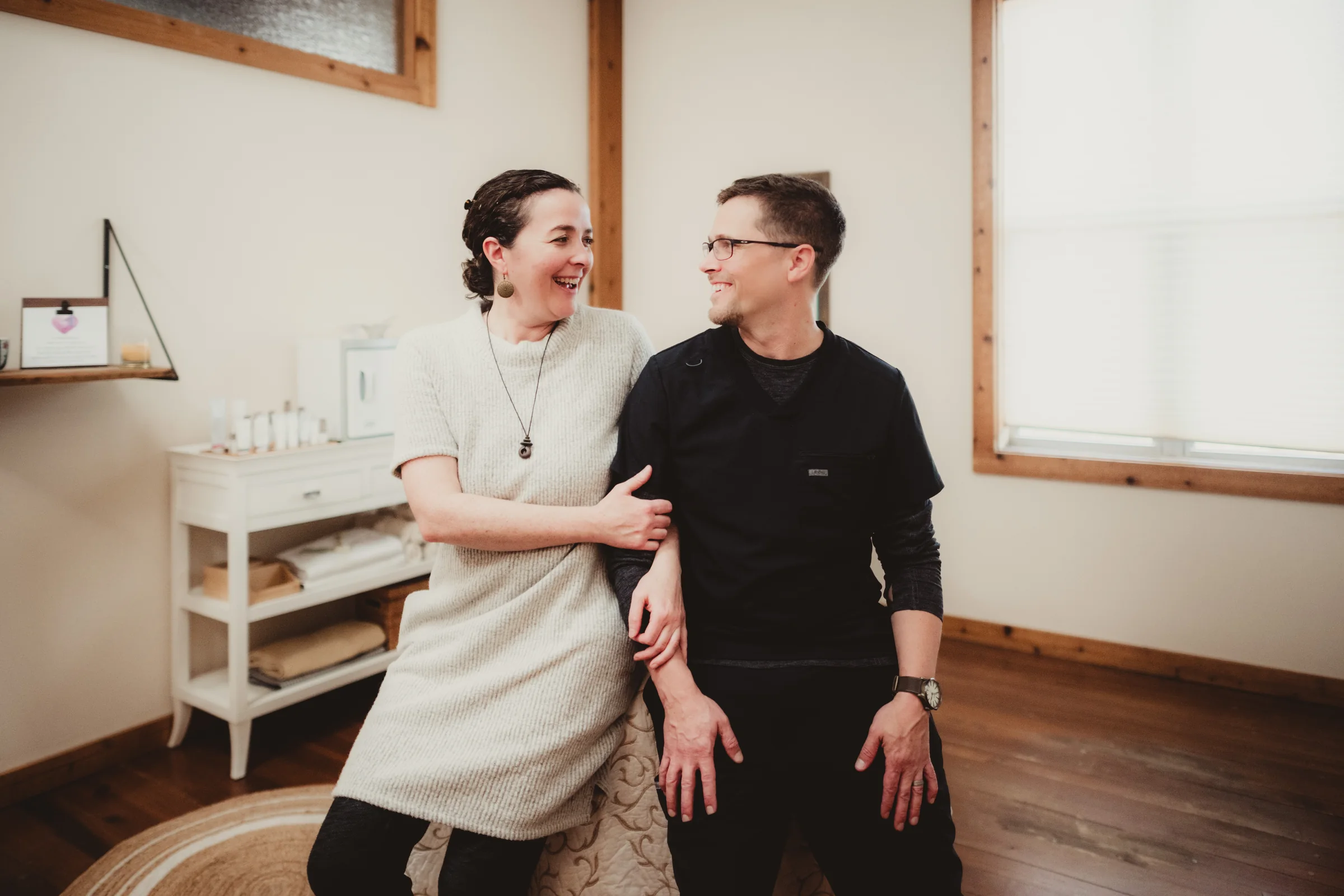 Two people laugh together while seated in a bright workspace.